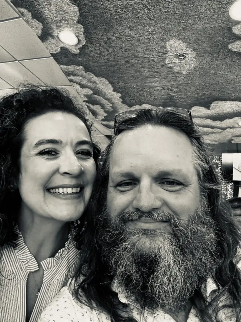 Justin Curatola smiling with a woman in a black-and-white selfie indoors.